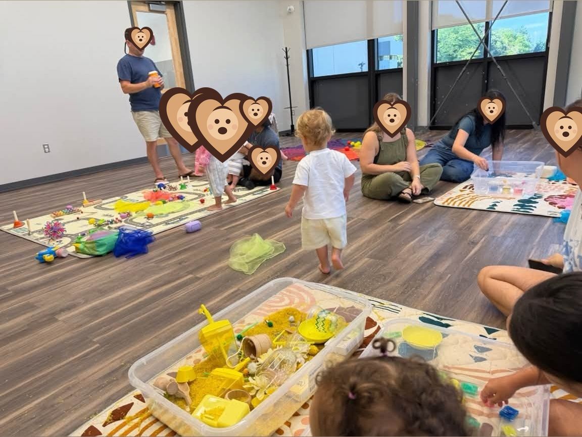 Caregivers sitting together while toddlers explore sensory bins nearby