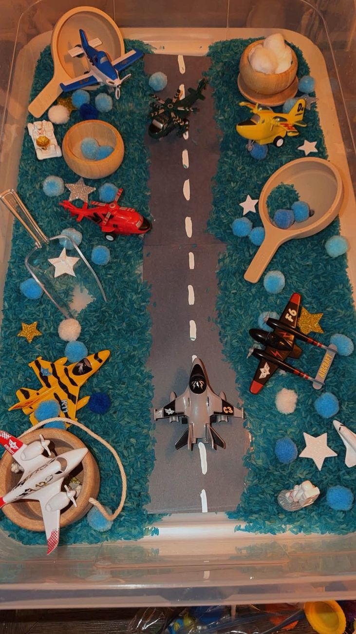 An airplane themed sensory tray with blue rice and a runway
