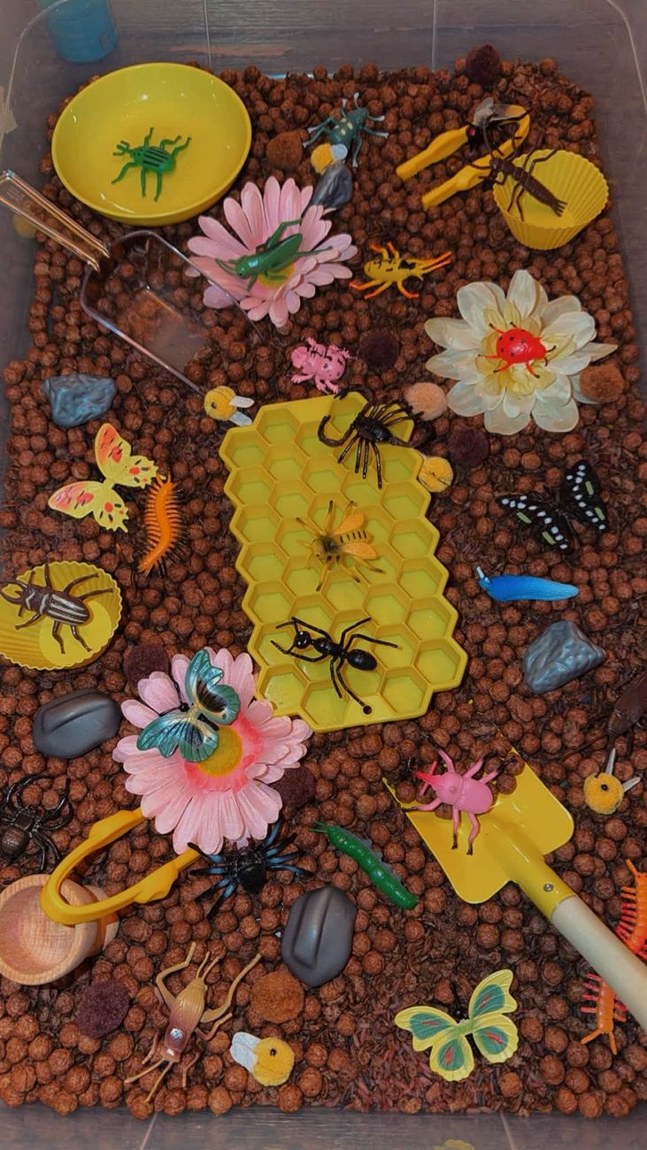 A bug themed sensory tray with cocoa cereal, insects, flowers and a honeycomb