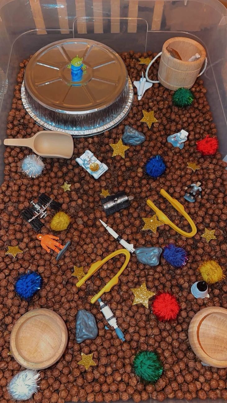 An outer space sensory tray with cocoa cereal, rockets and glitter stars