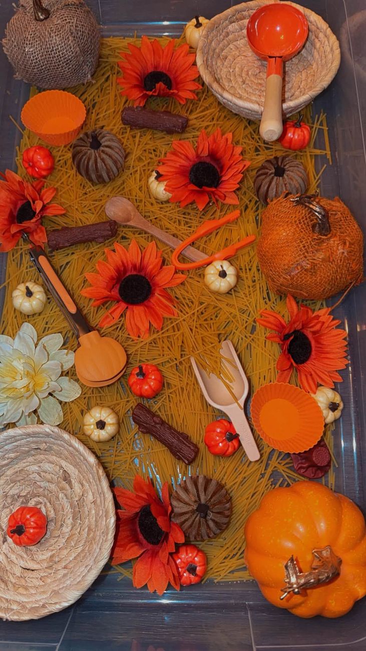 A fall sensory tray with dyed spaghetti, sunflowers, pumpkins and scoops