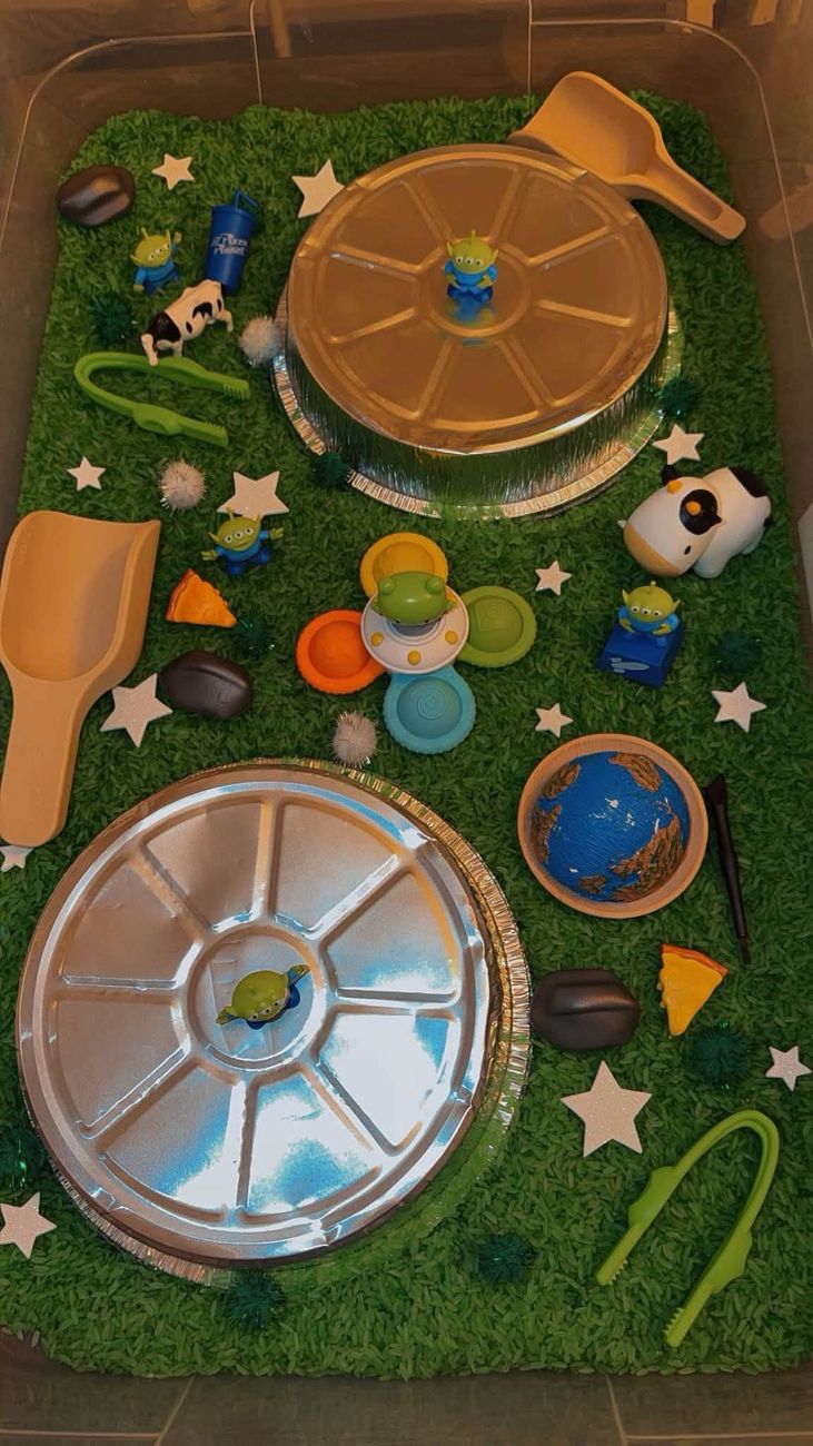 A space themed sensory tray with green rice, foil dishes and star confetti